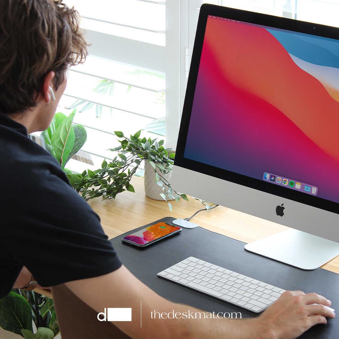 Man standing at a desk with an iMac 27 on it, using a Desk Mat Pro in his workflow