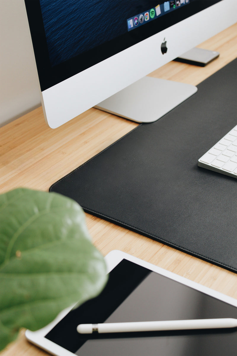 Modern office desk setup with computer monitor, keyboard, mouse, and tablet on a wooden surface.