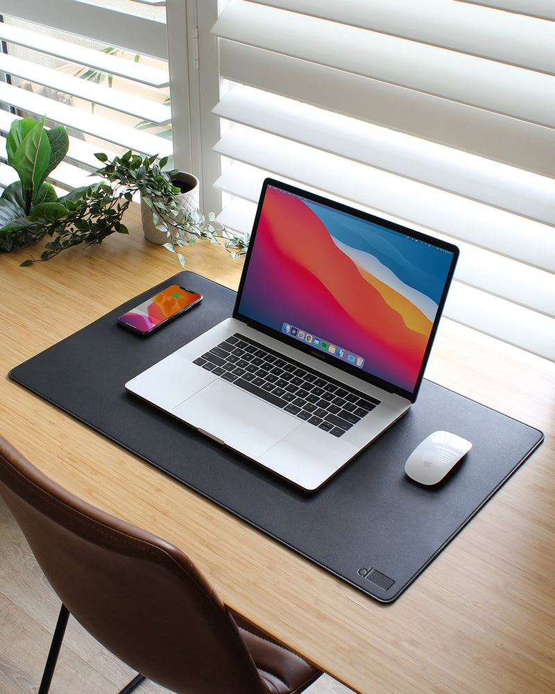 Laptop on a desk with a mouse and phone, on a large black mouse pad.