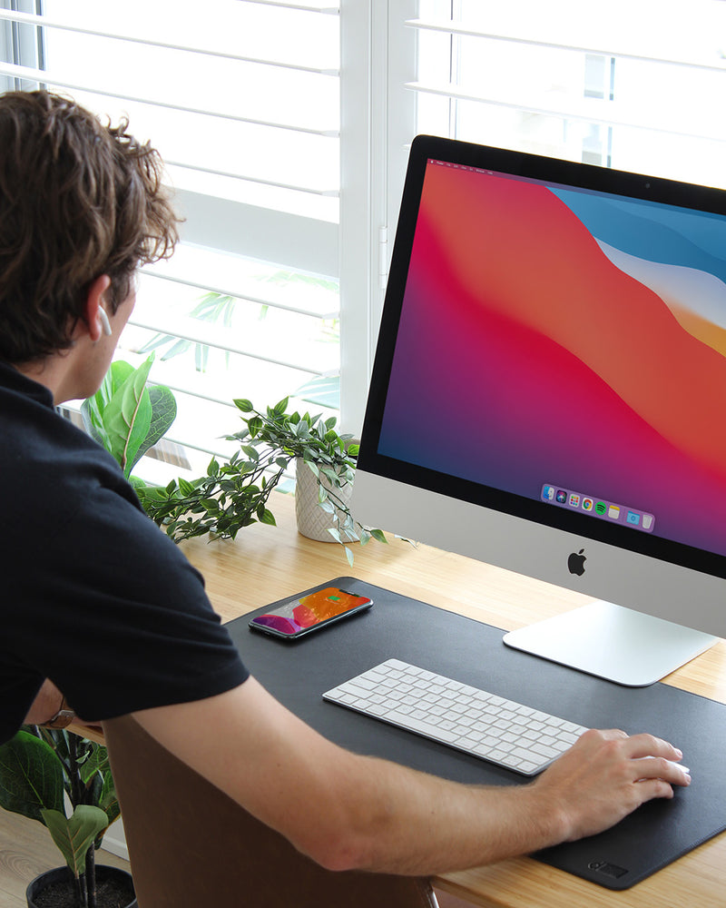 Person using a computer at a desk with a large monitor, keyboard, and smartphone.
