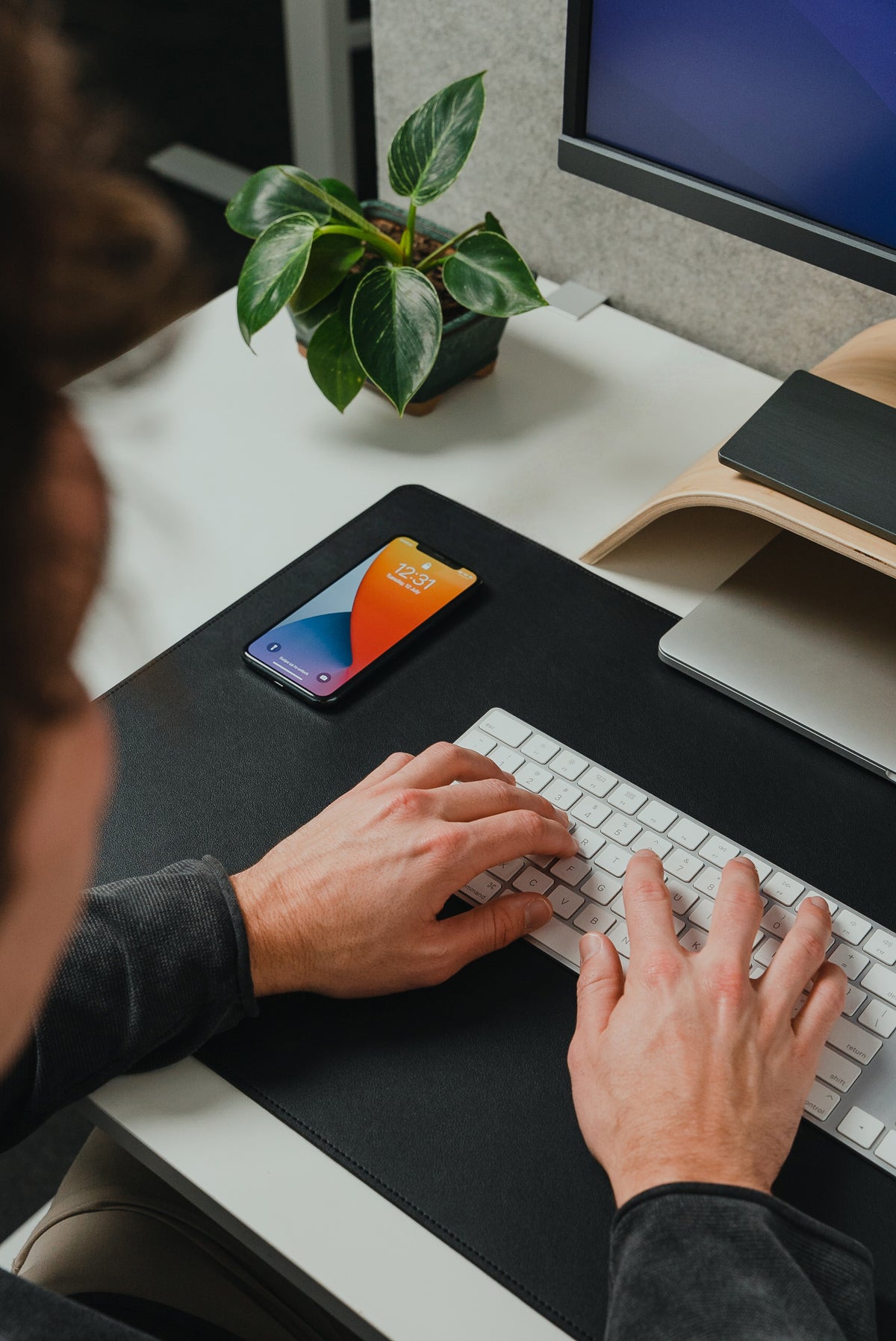 Person typing on a keyboard at a desk with a smartphone and plant in the background